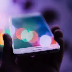 Dłoń trzyma telefon z kolorowymi światłami na ekranie. Chcesz wiedzieć, jak zrobić zdjęcie z filmu na telefonie?