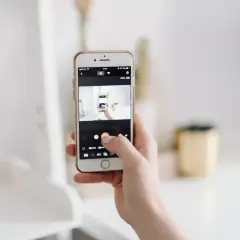 Dłoń trzyma smartfon, na ekranie którego widać aparat robiący zdjęcie. To jakby snapbridge po polsku, uchwycenie chwili.