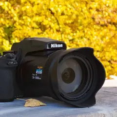 Czarny aparat Nikon P1000 z obiektywem na tle jesiennych, żółtych liści.
