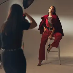 Sesja zdjęciowa w studio. Modelka w czerwonym stroju pozuje na stołku, fotograf robi zdjęcie. Zastanawiasz się, ile zarabia fotograf?