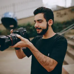 Młody mężczyzna z brodą trzyma w dłoniach swój pierwszy aparat Canon EOS 6D, gotowy do uchwycenia niezwykłych chwil.