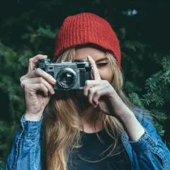 Dziewczyna w czerwonej czapce i dżinsowej kurtce trzyma aparat, gotowa do uchwycenia piękna przyrody. To jej dzień fotografa.