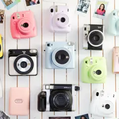 Różne rodzaje aparatów fotograficznych Instax w jaskrawych kolorach, ułożone na białym tle, otoczone odbitkami zdjęć.