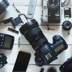 Rozłożone na białym tle aparaty fotograficzne, obiektywy i lampy błyskowe.