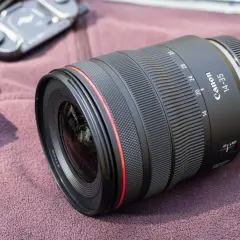 Obiektyw Canon 14-35mm, idealny do krajobrazu, leży na miękkim materiale obok akcesoriów fotograficznych.