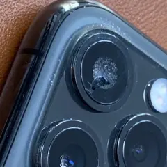 Zbliżenie na pęknięte szkło aparatu iPhone'a na brązowym tle.
