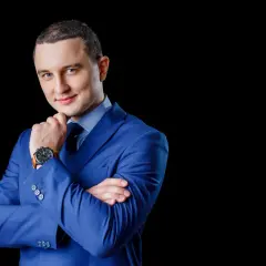 Mężczyzna w niebieskiej marynarce, z rękami skrzyżowanymi na piersi, zastanawia się, jak wkleić zdjęcie do CV.