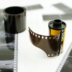 Kasetka z kliszą fotograficzną i rozwinięty negatyw na białym tle.
