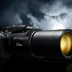 Czarny aparat Nikon Coolpix P1000 z potężnym obiektywem 24-3000mm, gotowy do uchwycenia odległych detali na tle burzowego nieba.