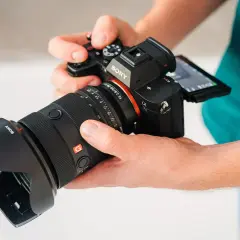 Dłonie trzymają aparat Sony a7r5 z obiektywem.