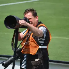Fotograf z aparatem na monopody, gotowy do uchwycenia akcji na boisku.