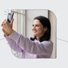 Uśmiechnięta dziewczyna robi selfie telefonem, jakby korzystała z automatu do robienia zdjęć do dowodu.