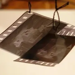 Wywoływanie zdjęć z kliszy. Dwie taśmy filmowe z widocznymi klatkami, wiszące na czarnych nitkach.