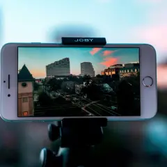 iPhone nagrywa timelapse miasta o zachodzie słońca. Widać budynki, drzewa i ulicę.
