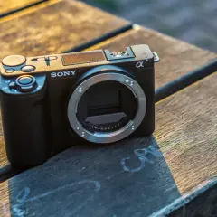 Czarny aparat Sony Alpha ZV-E10 bez obiektywu leży na drewnianym stole.