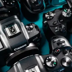 Zbliżenie na kilka aparatów fotograficznych marek Canon, Nikon i Sony ułożonych na niebieskim tle.