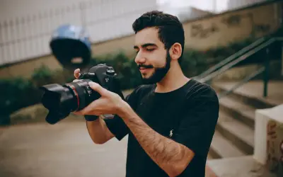 Młody mężczyzna z brodą trzyma w dłoniach swój pierwszy aparat Canon EOS 6D, gotowy do uchwycenia niezwykłych chwil.
