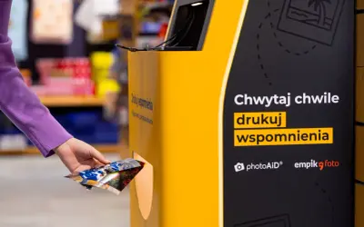 Ręka wkłada zdjęcia do automatu, by wydrukować wspomnienia w Empiku.
