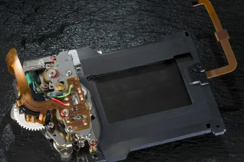 Mechanizm migawki szczelinowej aparatu z taśmami flex i elementami elektronicznymi.