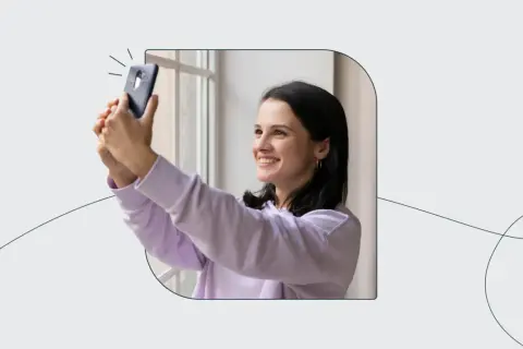 Uśmiechnięta dziewczyna robi selfie telefonem, jakby korzystała z automatu do robienia zdjęć do dowodu.
