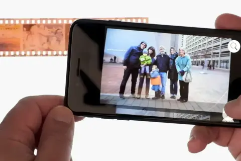 Telefon wyświetla zdjęcie rodziny, obok negatyw filmowy. Dowiedz się, jak odwrócić kolory zdjęcia na telefonie, by uzyskać ciekawy efekt.