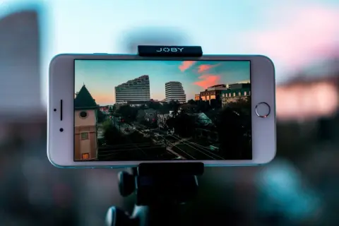 iPhone nagrywa timelapse miasta o zachodzie słońca. Widać budynki, drzewa i ulicę.