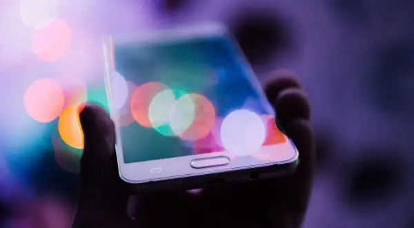 Dłoń trzyma telefon z kolorowymi światłami na ekranie. Chcesz wiedzieć, jak zrobić zdjęcie z filmu na telefonie?