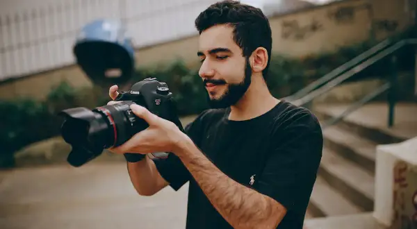 Młody mężczyzna z brodą trzyma w dłoniach swój pierwszy aparat Canon EOS 6D, gotowy do uchwycenia niezwykłych chwil.