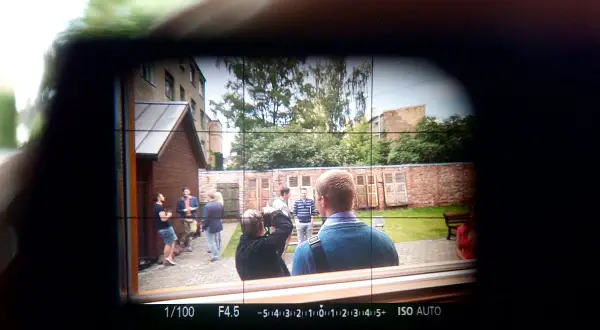 Obraz widoczny w wizjerze kamery: grupa ludzi na podwórku, jeden z nich robi zdjęcie.