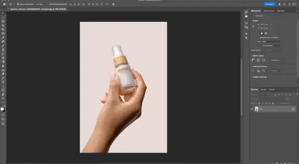 Dłoń trzymająca buteleczkę kosmetyku na jasnym tle. Program Photoshop pokazuje narzędzia, jak usunąć tło ze zdjęcia, aby wyizolować produkt.