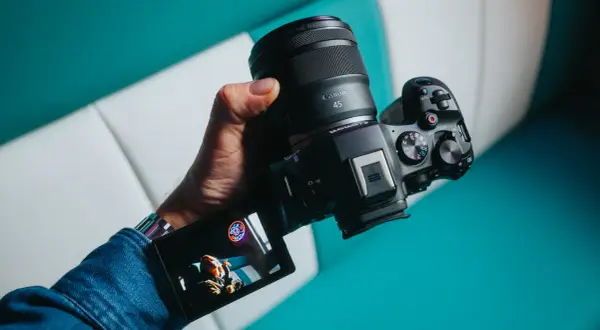 Dłoń trzyma aparat Canon z obiektywem RF 45mm. Wyświetlacz pokazuje zdjęcie.