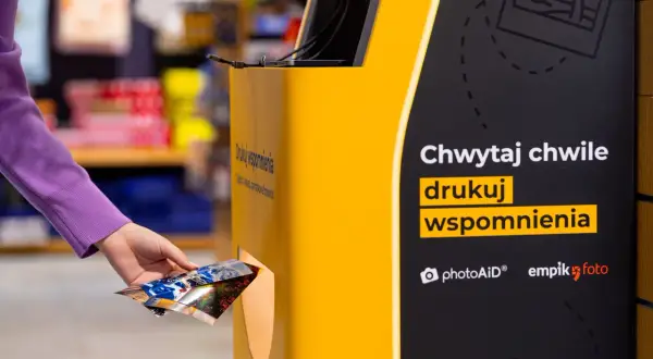 Ręka wkłada zdjęcia do automatu, by wydrukować wspomnienia w Empiku.