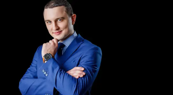 Mężczyzna w niebieskiej marynarce, z rękami skrzyżowanymi na piersi, zastanawia się, jak wkleić zdjęcie do CV.