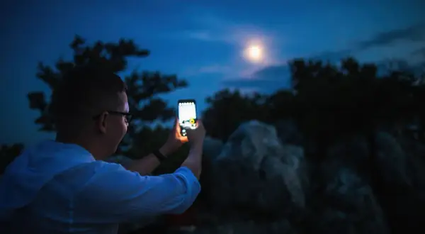 Chłopak z telefonem próbuje uchwycić księżyc. Oto jak zrobić zdjęcie księżyca telefonem, by było magiczne!