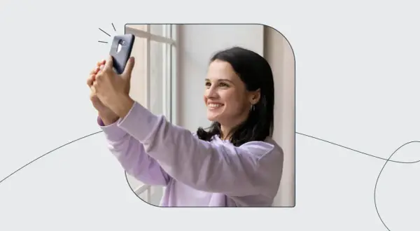 Uśmiechnięta dziewczyna robi selfie telefonem, jakby korzystała z automatu do robienia zdjęć do dowodu.