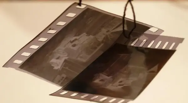 Wywoływanie zdjęć z kliszy. Dwie taśmy filmowe z widocznymi klatkami, wiszące na czarnych nitkach.