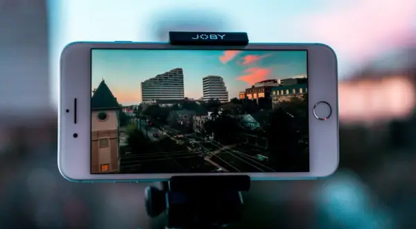 iPhone nagrywa timelapse miasta o zachodzie słońca. Widać budynki, drzewa i ulicę.