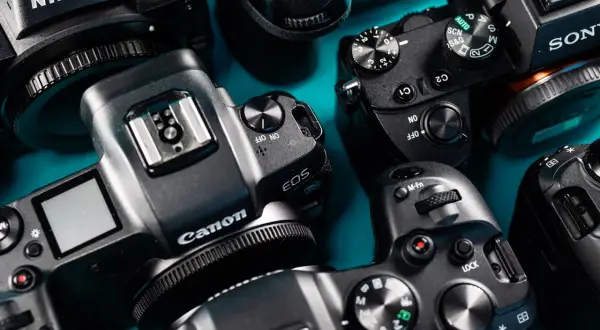 Zbliżenie na kilka aparatów fotograficznych marek Canon, Nikon i Sony ułożonych na niebieskim tle.