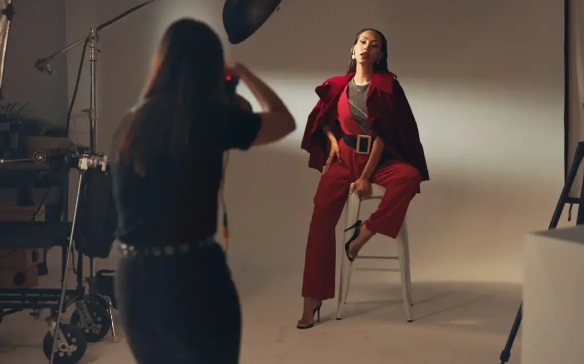 Sesja zdjęciowa w studio. Modelka w czerwonym stroju pozuje na stołku, fotograf robi zdjęcie. Zastanawiasz się, ile zarabia fotograf?