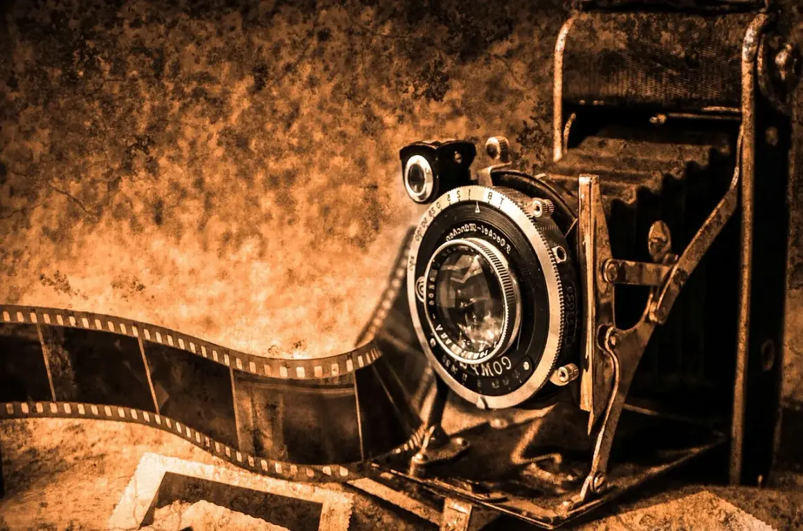 Antyczna kamera i rolka kliszy, świadkowie pierwszych fotografii, w sepia tonacji.