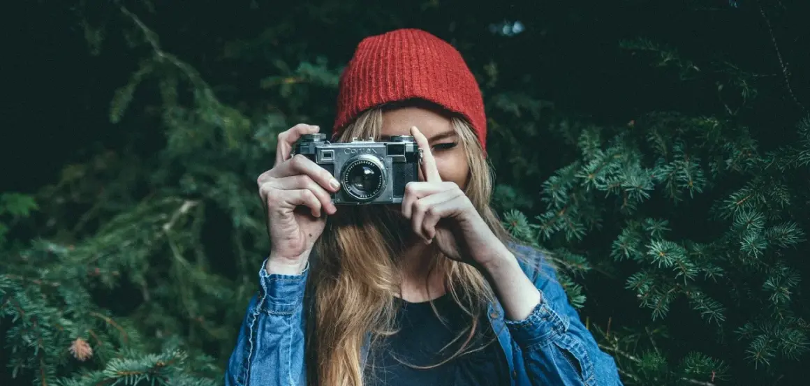 Dziewczyna w czerwonej czapce i dżinsowej kurtce trzyma aparat, gotowa do uchwycenia piękna przyrody. To jej dzień fotografa.