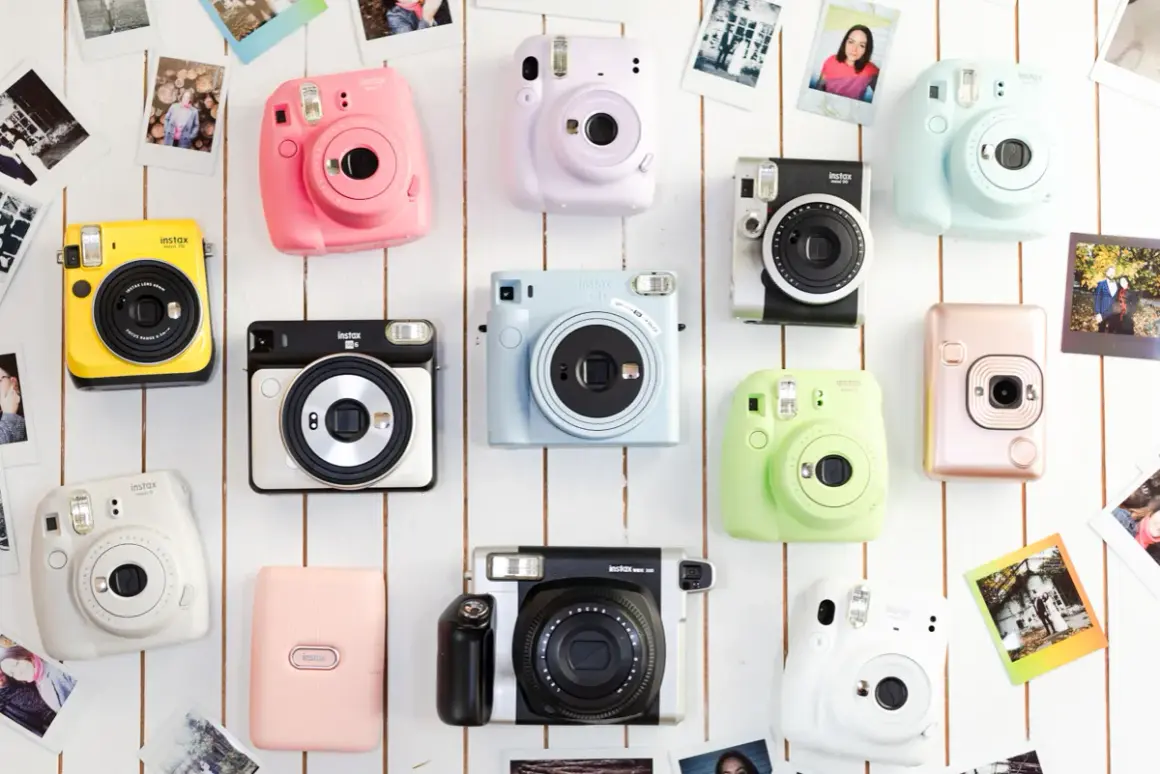 Różne rodzaje aparatów fotograficznych Instax w jaskrawych kolorach, ułożone na białym tle, otoczone odbitkami zdjęć.