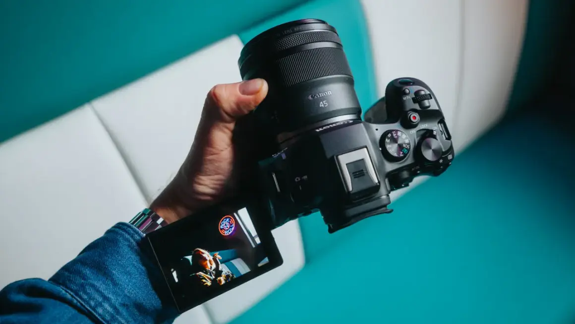 Dłoń trzyma aparat Canon z obiektywem RF 45mm. Wyświetlacz pokazuje zdjęcie.