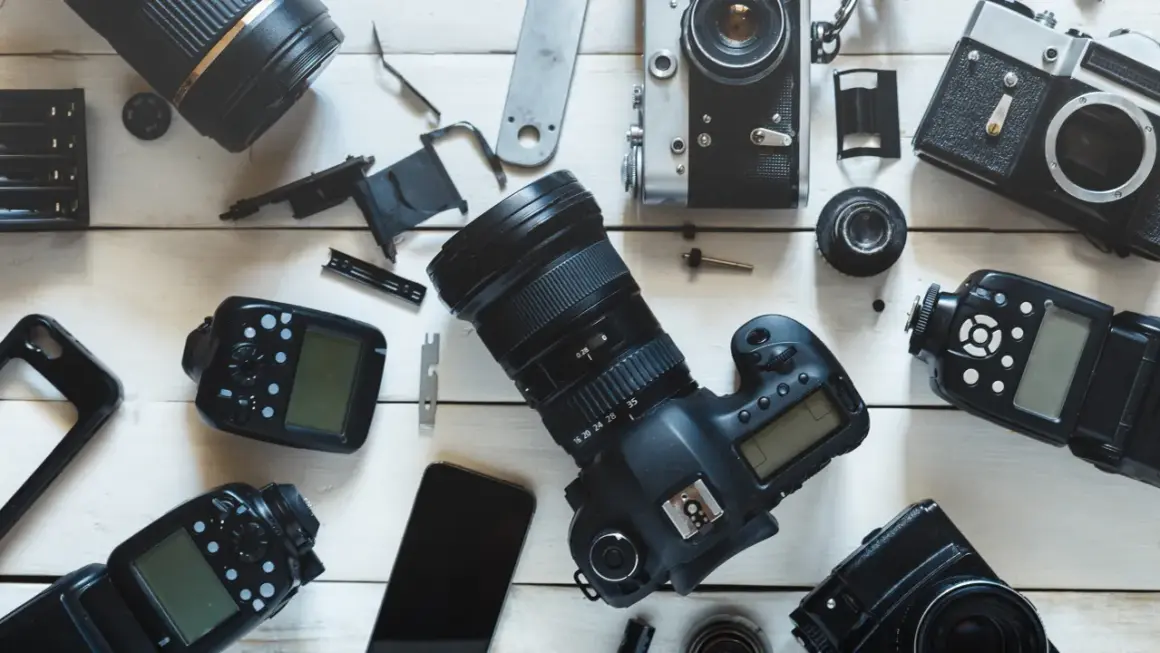 Rozłożone na białym tle aparaty fotograficzne, obiektywy i lampy błyskowe.