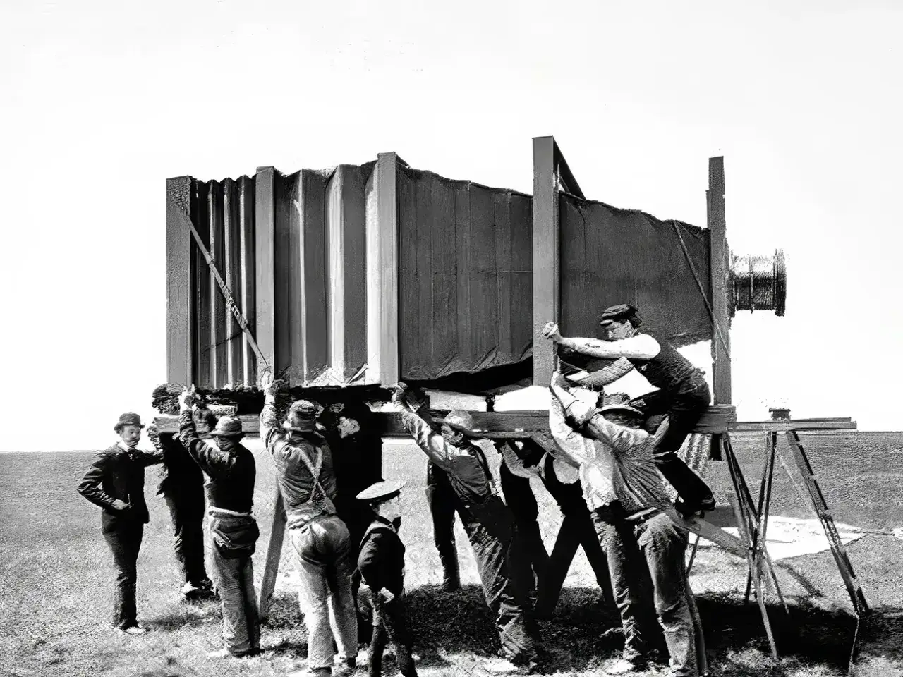Grupa mężczyzn w historycznych strojach montuje gigantyczny aparat fotograficzny, jakby właśnie wynaleziono aparat fotograficzny.