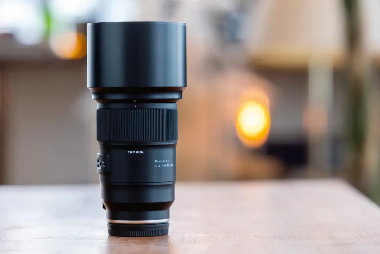 Obiektyw Tamron 90mm F/2.8 Di III MACRO VXD, idealny do makro zdjęć, stoi na drewnianym blacie.