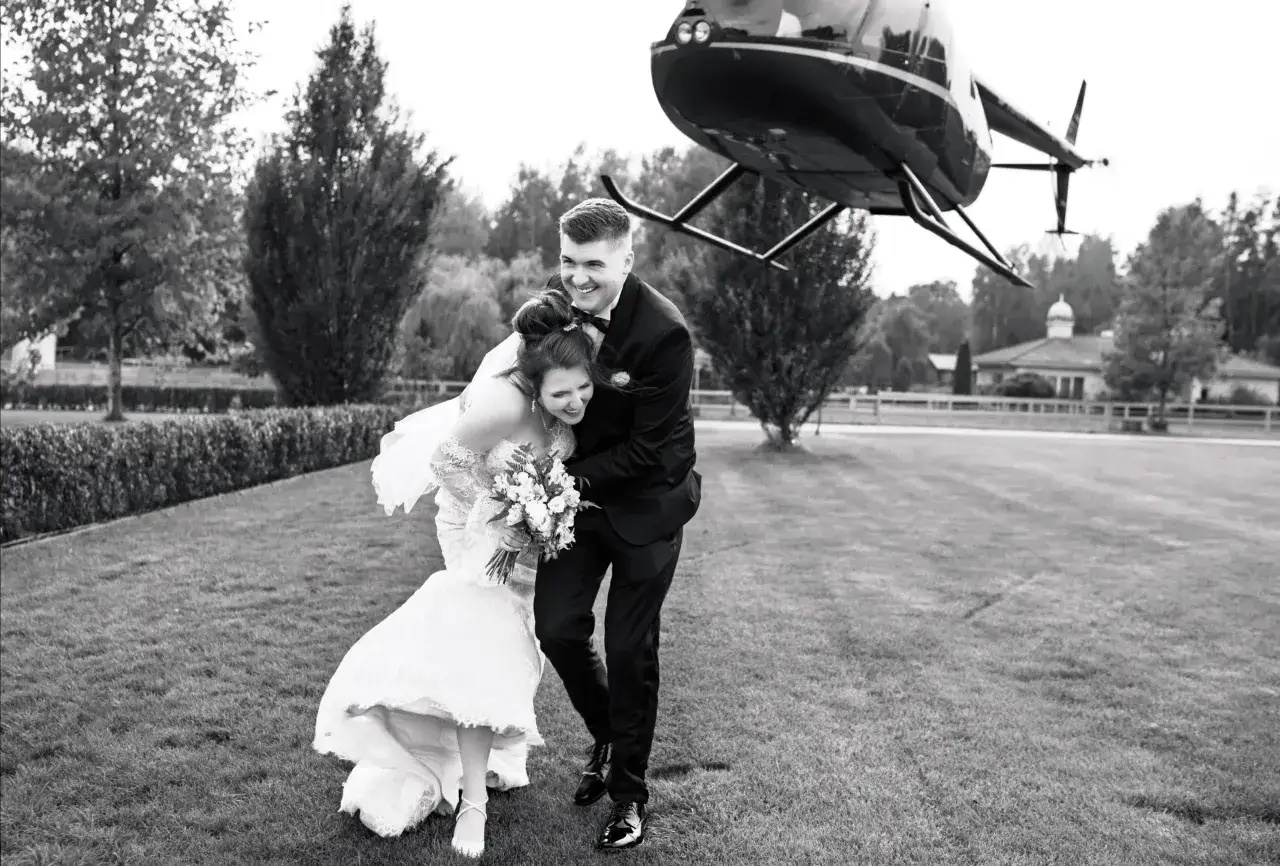 Szczęśliwa para młoda z bukietem kwiatów, tuż obok lądującego helikoptera. Zastanawiasz się, ile kosztuje fotograf na wesele z taką oprawą?