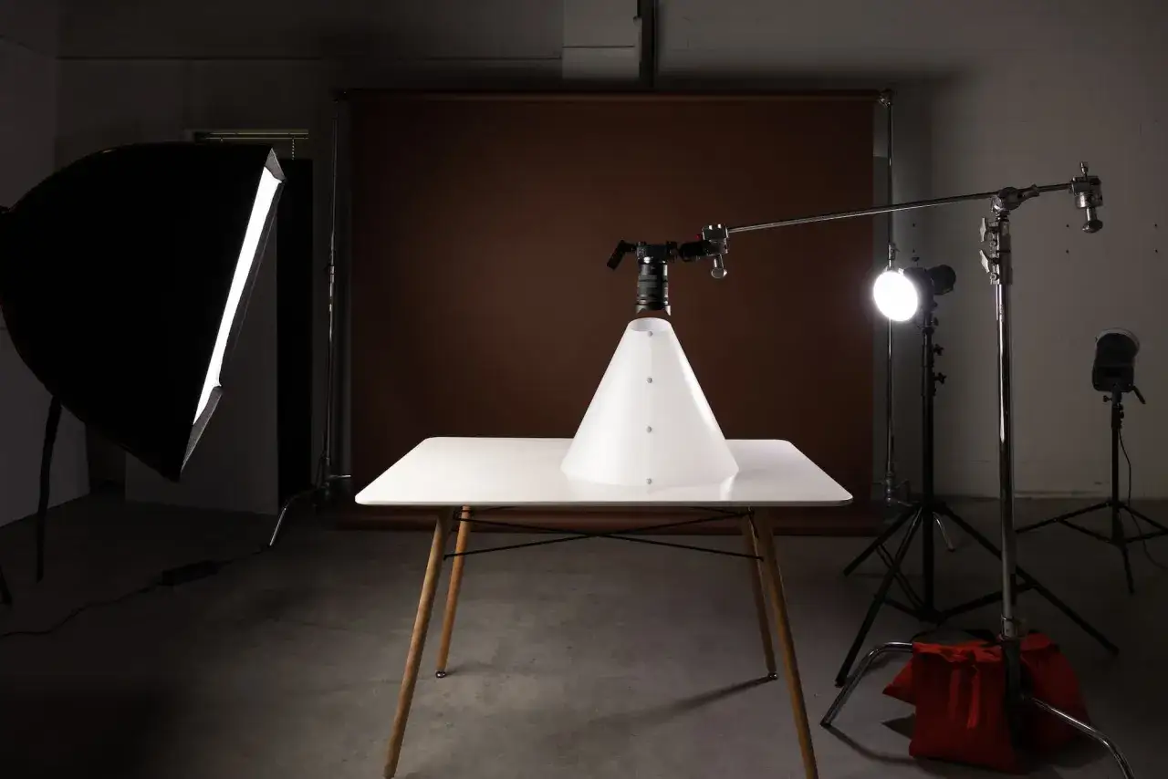 Ustawienie aparatu do fotografii produktowej. Biały stożek na stole, oświetlony softboxem i lampami studyjnymi.