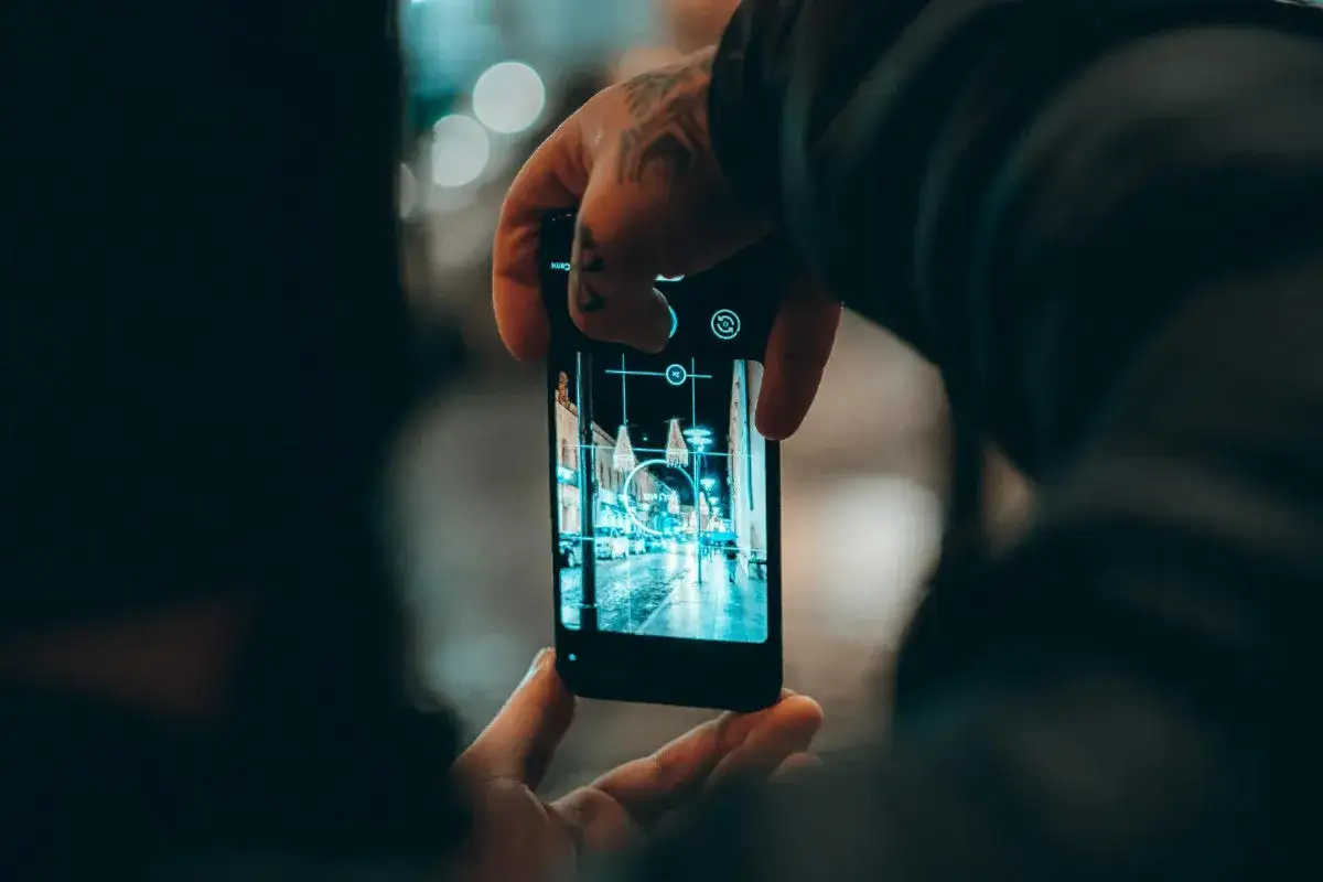 Nocne miasto uchwycone przez obiektyw smartfona. Światła uliczne odbijają się na mokrej nawierzchni, tworząc magiczny klimat. To świetna fotografia mobilna.