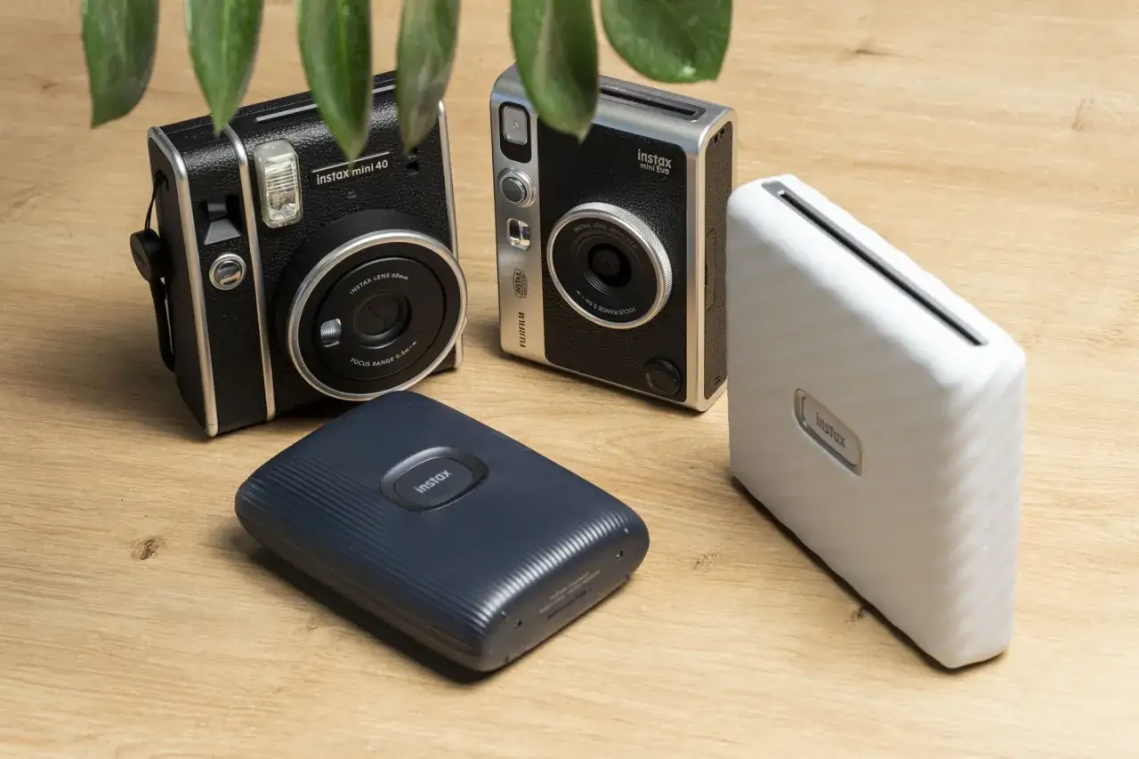 Dwa aparaty Instax Mini 40 i Mini Evo oraz dwa mobilne drukarki Instax na drewnianym tle.